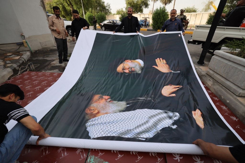 Men prepare to hang a huge portrait of Iran's late president Ebrahim Raisi (R) and the Islamic republic's supreme leader outside the Iranian embassy in Baghdad during a condolences service on May 20, 2024 for the president and his entourage, who were killed in a helicopter crash in Iran the previous day. (Photo by AHMAD AL-RUBAYE / AFP)