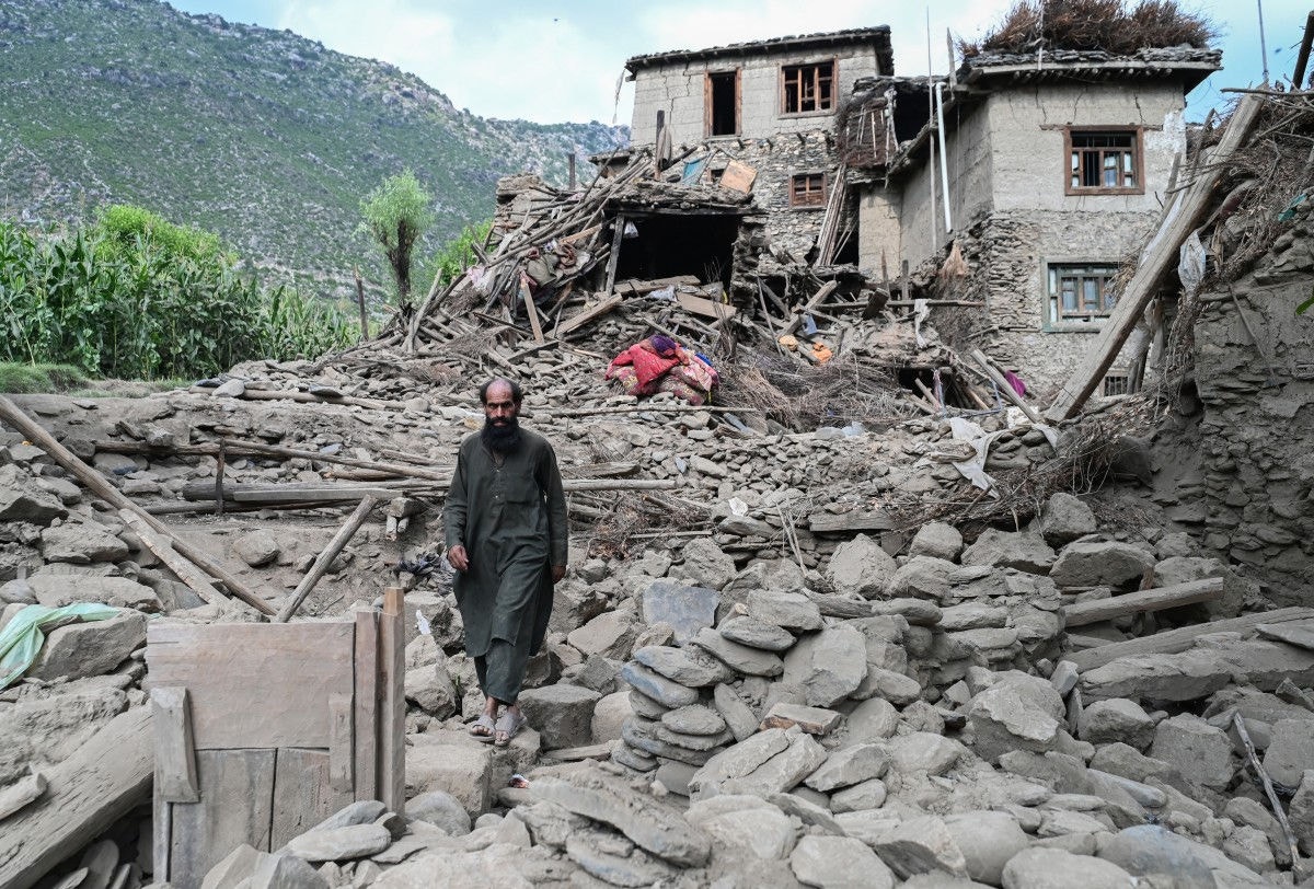 Um afegão caminha em frente a uma casa destruída após terremotos na vila de Mazar Dara, em Nurgal, ao leste do Afeganistão