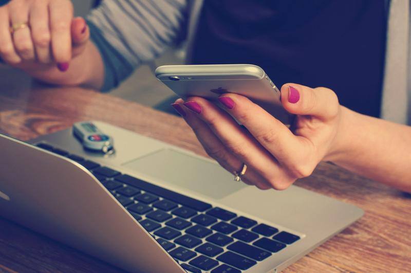Pessoa segura um smartphone diante de um notebook