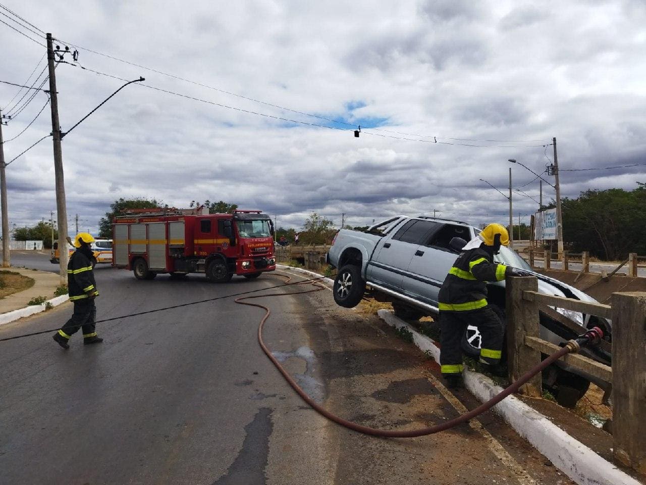 Foto mostra a caminhonete pendurada sobre o córrego enquanto militares do bombeiros atuavam no combate ao incêndio provocado pela batida