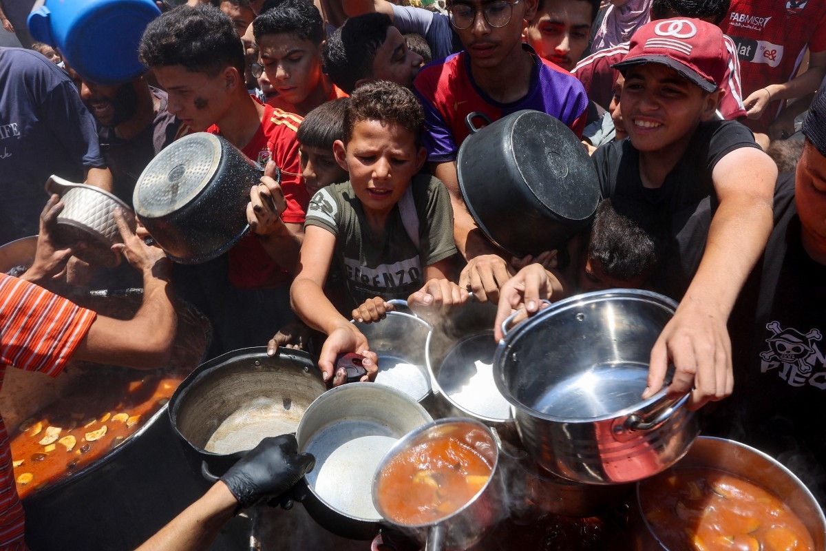 Palestinians try to get food at a charity kitchen providing hot meals in Rimal neighbourhood in Gaza City on June 18, 2025, amid the ongoing war between Israel and the Palestinian Hamas movement. The humanitarian situation in Gaza remains dire despite aid beginning to trickle back into the territory after a more than two-month Israeli blockade. Food security experts say starvation is looming for one in five people. Israel has also intensified its military offensive in what it says is a renewed push to destroy Hamas, whose October 7, 2023 attack triggered the war. (Photo by Omar AL-QATTAA / AFP)