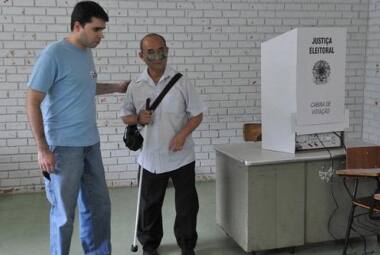 José Augusto, deficiente visual, recebe o auxílio de um mesário ao votar no Distrito Federal