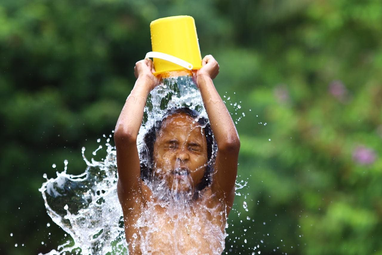 Imagem ilustrativa de uma criança se refrescando com um balde de água