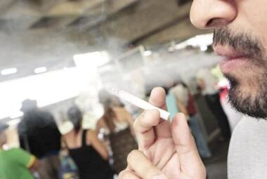 Foco Fumante com seu cigarro em ambiente tabagista rodeado de não-fumantes, segundos da lista a serem prejudicados pela fumaça