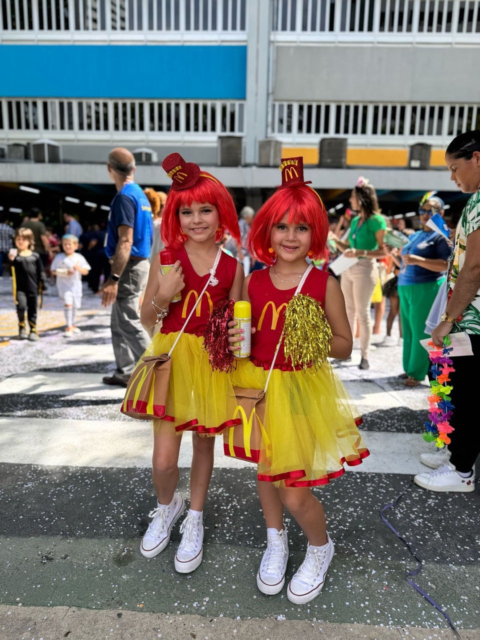 As garotas  saíram para a folia vestidas com uma camiseta vermelha, estampando o M da marca, saia amarela e peruca vermelha