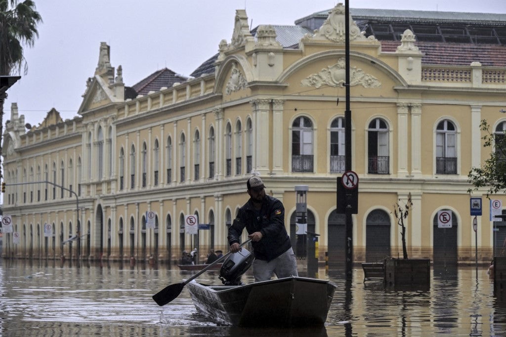 A man navigates a boat through a flooded street in front of the public market in downtown Porto Alegre, Rio Grande do Sul State, Brazil, on May 19, 2024. Porto Alegre, the Brazilian metropolis left submerged after torrential rains, had been lulled into a "false sense" of security by a vast but aging system of flood defenses, an urban drainage engineer told AFP. Leomar Teichmann said a network of dikes, levees and a massive wall was meant to protect about 40 percent of the capital city of Rio Grande do Sul state in southern Brazil, where 150 people have died and hundreds of thousands were forced from their homes. (Photo by Nelson ALMEIDA / AFP)
