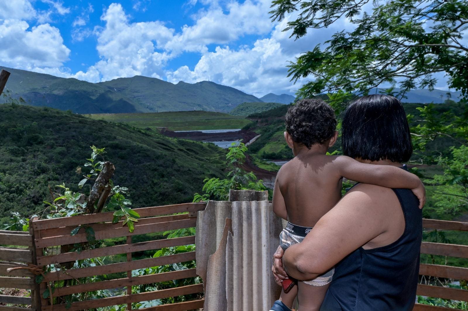 Com o neto de 2 anos no colo, Rosemeire observa, do quintal da casa de seu filho, a barragem que ameaça o distrito