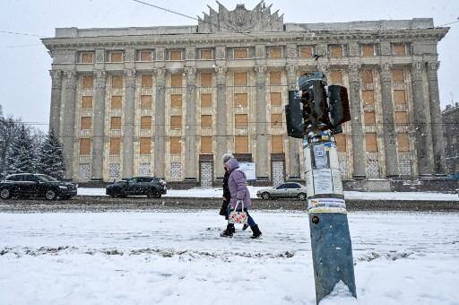 Mulheres caminham sob a neve em frente ao prédio danificado da Administração Estatal Regional de Kharkiv, em meio à invasão russa da Ucrânia