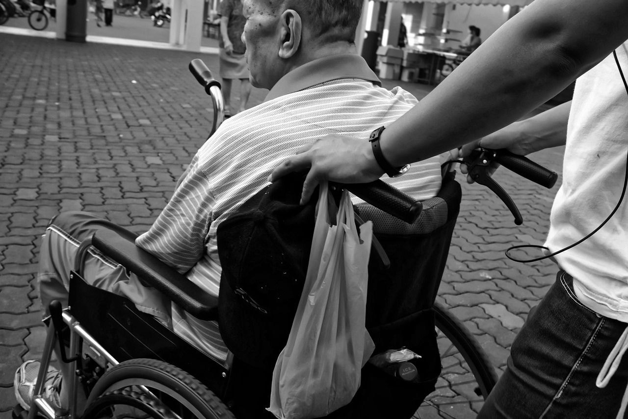 Foto ilustrativa mostra idoso sendo empurrado em cadeira de rodas