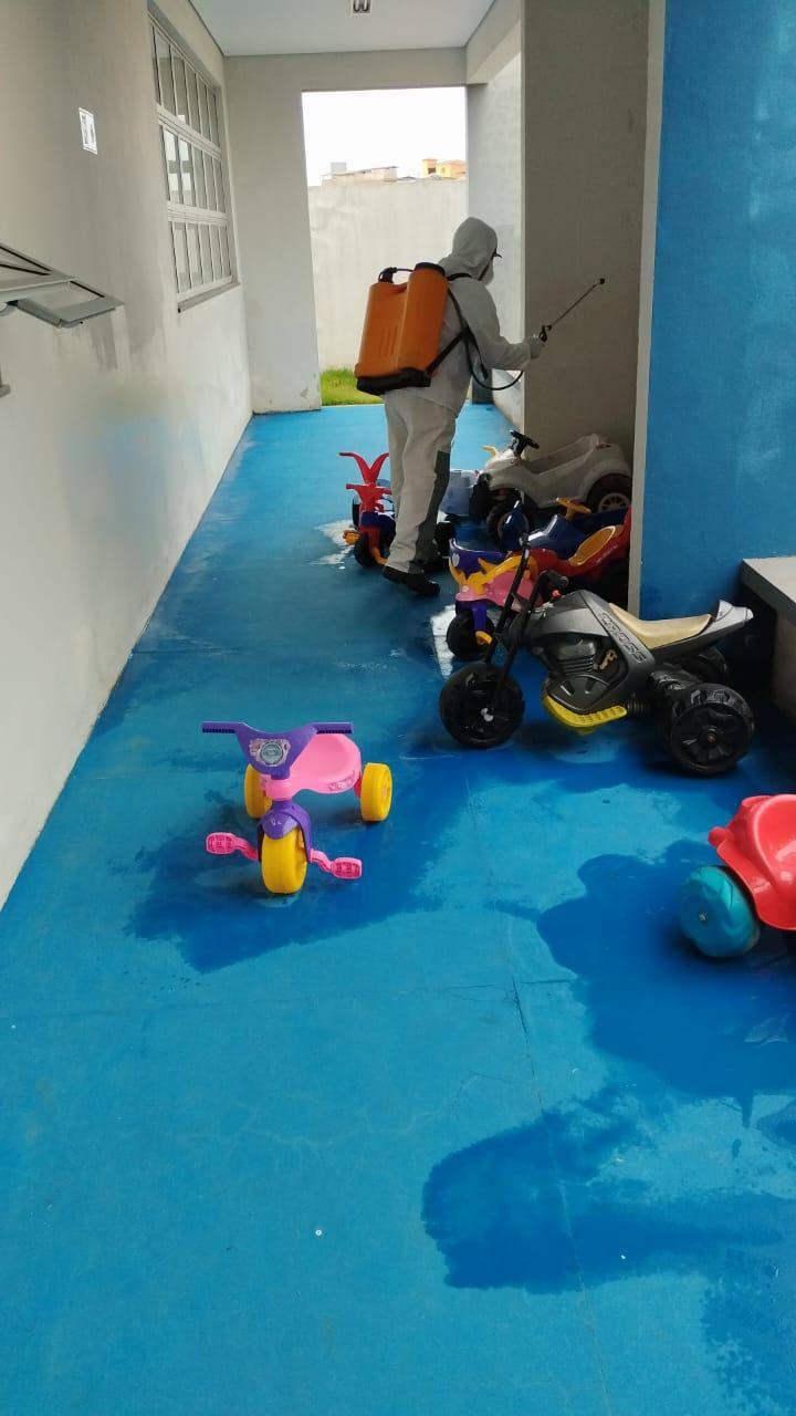 Foto mostra trabalhador do município jogando água sanitária com uma bomba sobre brinquedos na escola