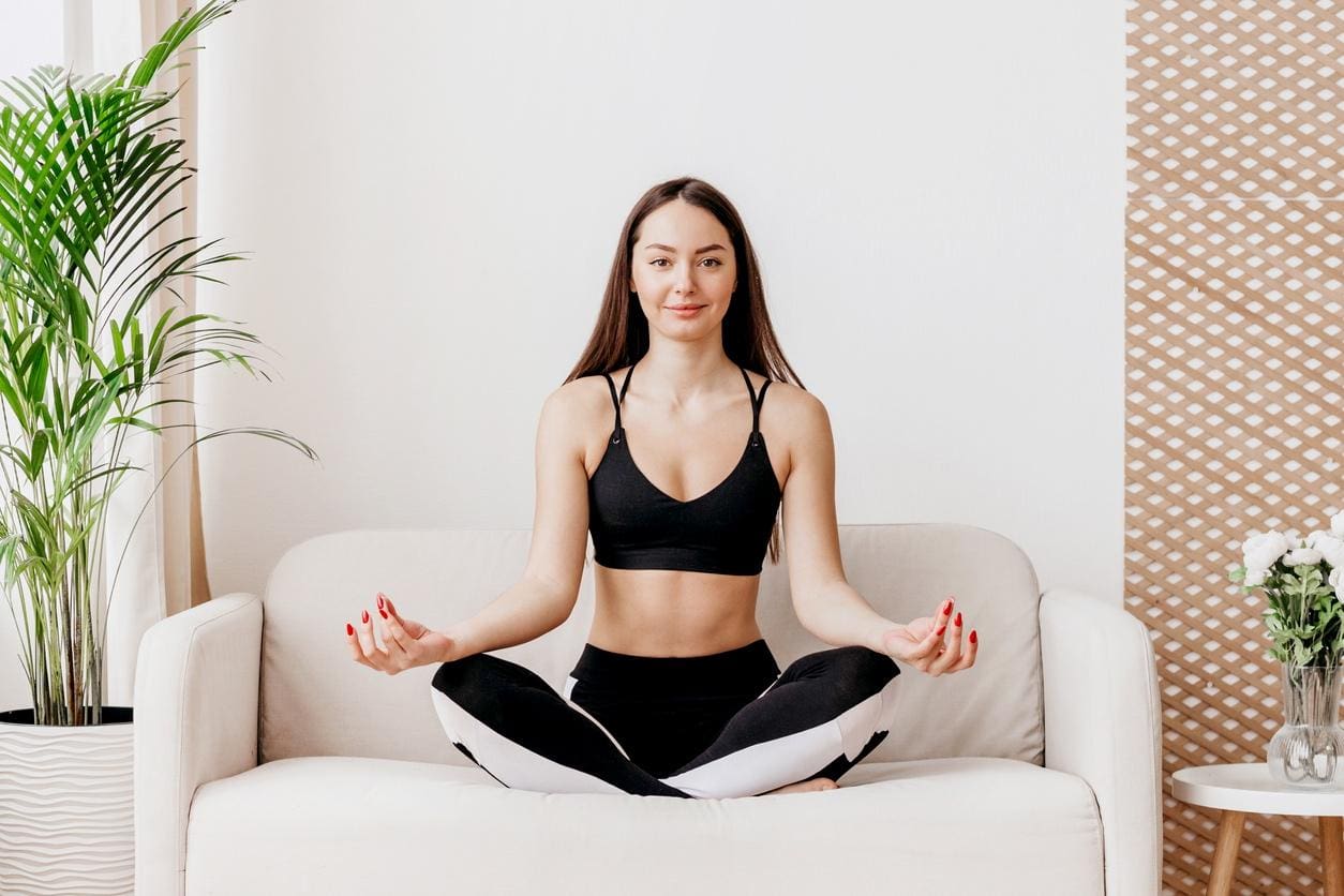 mulher meditando sentada no sofá posição flor de lotus de olhos abertos