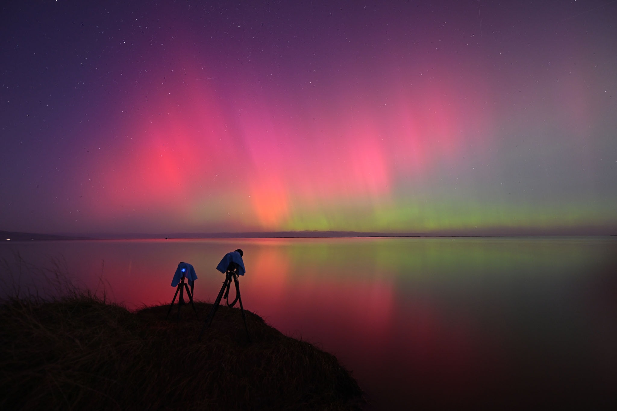 A photographer's camera setup is seen as the Aurora Australis, also known as the Southern Lights, glow on the horizon over waters of Lake Ellesmere on the outskirts of Christchurch on May 11, 2024. The most powerful solar storm in more than two decades struck Earth, triggering spectacular celestial light shows from Tasmania to Britain -- and threatening possible disruptions to satellites and power grids as it persists into the weekend. (Photo by Sanka Vidanagama / AFP)