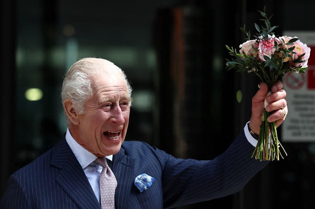 O rei Charles III segurando um ramo de flores e acenando para a multidão em Londres