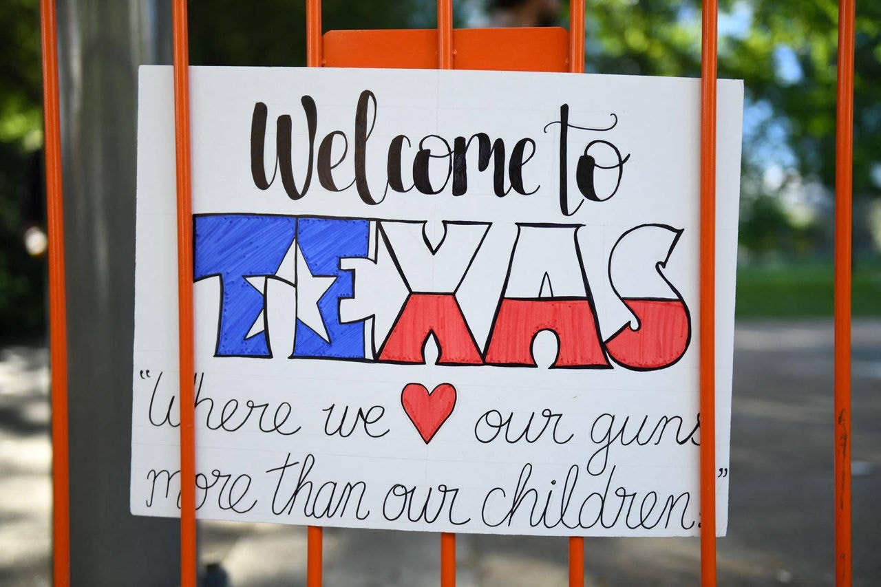 Cartaz irônico diz "Bem-vindo ao Texas, onde nós amamos mais as nossas armas do que nossas crianças"