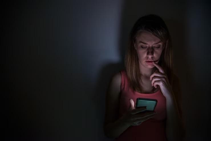 Imagem ilustrativa de mulher olhando o celular em um fundo preto
