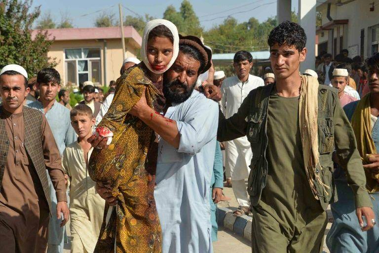 Homem carrega menina ferida em ataque com carro-bomba no distrito de Ghani Khel, na província afegã de Nangarhar