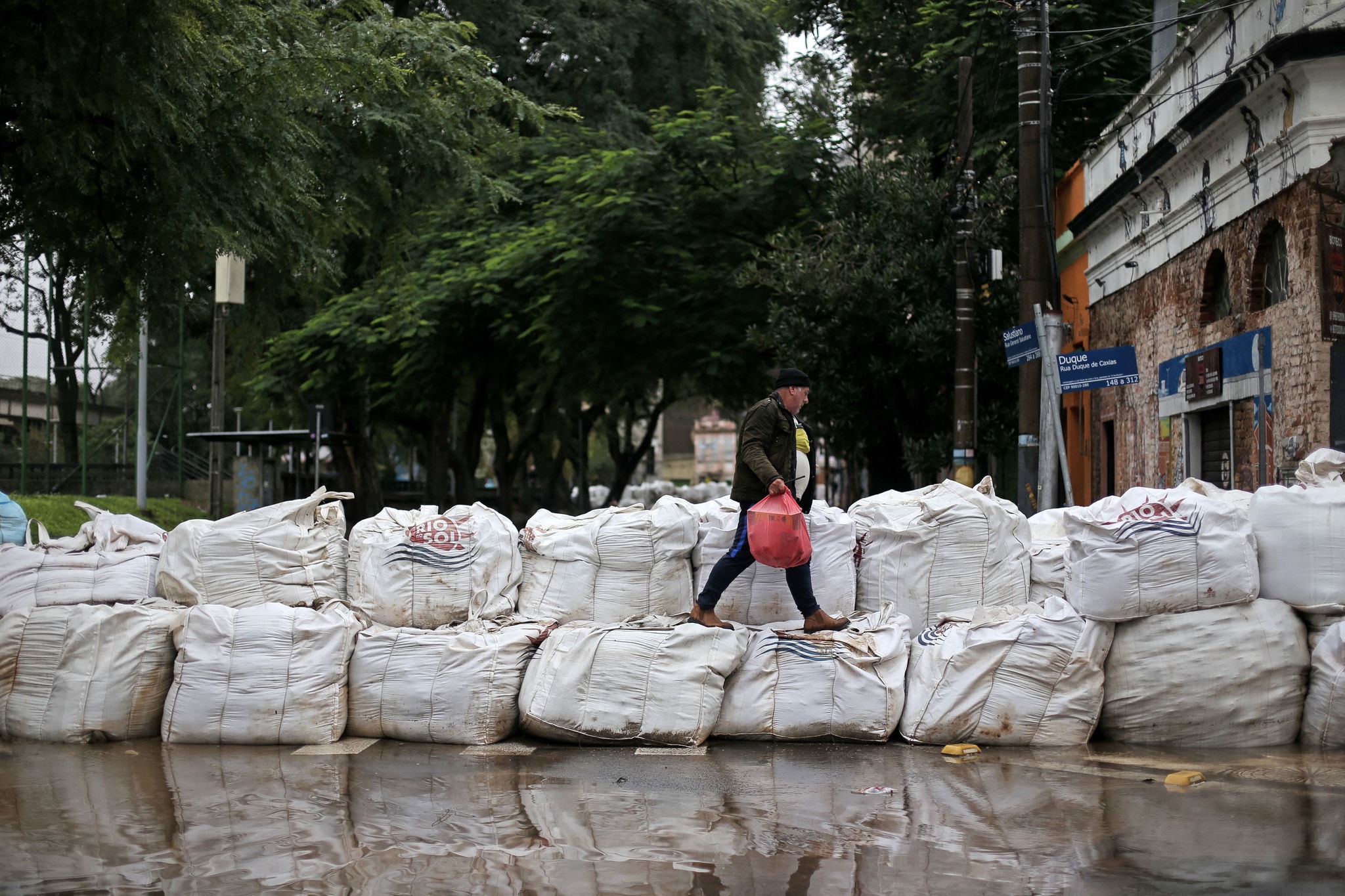 A man walks on a barrier made with bags full of rocks and sand at the historical city center of Porto Alegre, Rio Grande do Sul, Brazil on May 12, 2024. New rains in waterlogged southern Brazil are expected to be heaviest between Sunday and Monday, authorities have warned, bringing fresh misery to victims of flooding that has killed 136 people and left 806 injured and 125 missing so far. (Photo by Anselmo CUNHA / AFP)