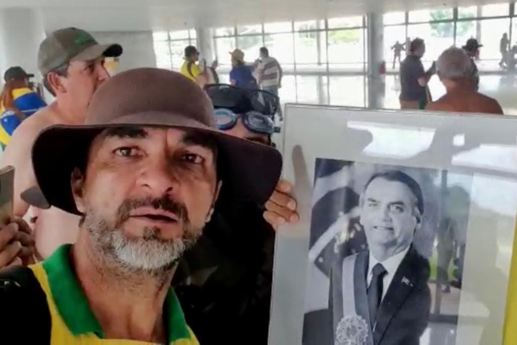 Alcimar Francisco da Silva exibe quadro com foto do ex-presidente Jair Bolsonaro, durante ataque ao Planalto: “Ó, meu herói aqui, ó Estamos na casa dele aqui, ó, na nossa casa, aqui, ó, na nossa casa”