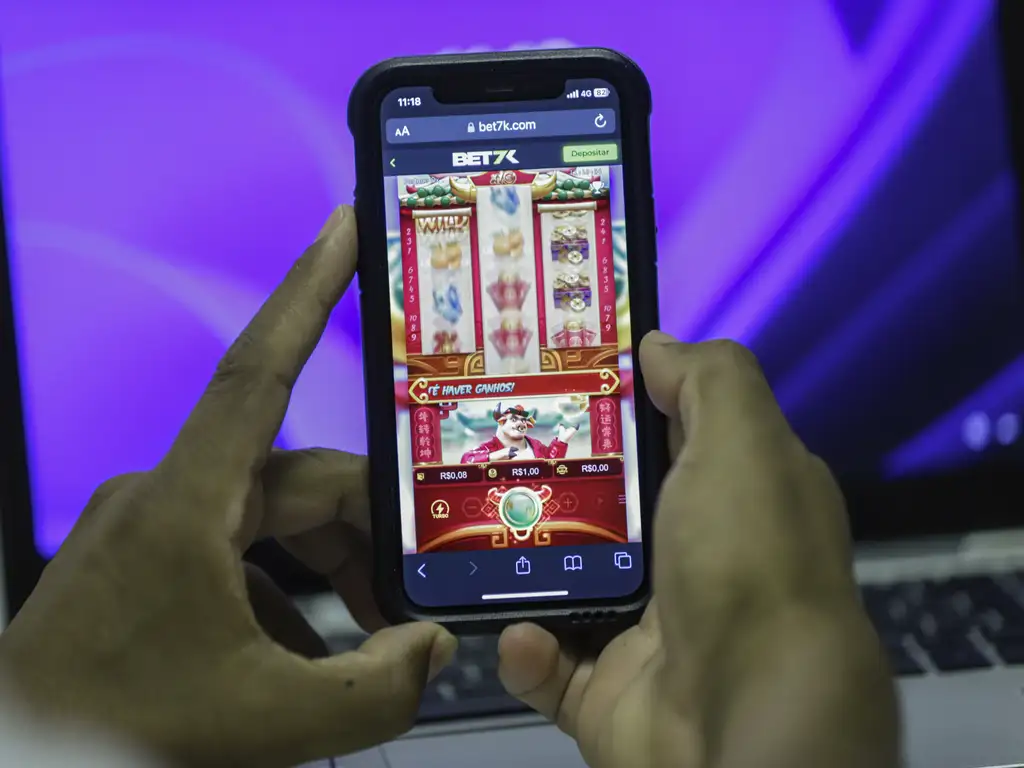 Um homem segura celular mostrando uma plataforma de um jogo online