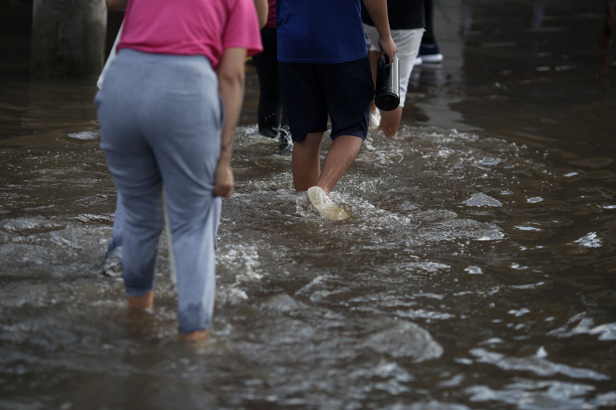 People cross a flooded street in the Sarandi neighborhood in Porto Alegre, Rio Grande do Sul state, Brazil, on May 5, 2024. The challenge is titanic and against the clock: authorities and neighbours are trying to avoid an even greater tragedy than the one already experienced in the Brazilian state of Rio Grande do Sul, where 66 people died and 80,000 were displaced by the floods, according to the authorities. (Photo by Anselmo Cunha / AFP)