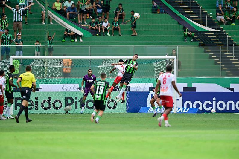 No centro da foto, o zagueiro Éder, do América, disputa a bola com o jogador do Villa Nova