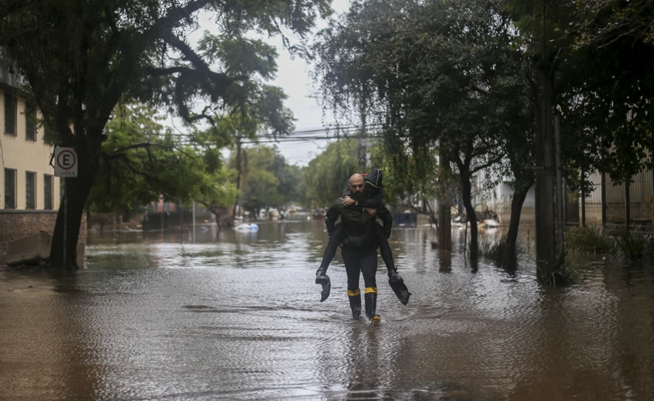 Um homem carrega sua mulher em meio à nova enchente em Porto Alegre