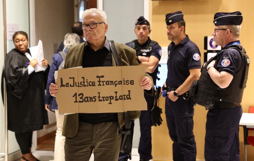 Homem segura placa com frase: "Justiça francesa: 13 anos atrasada"