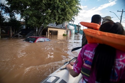Katiane Mello (R) leaves her flooded home in a boat navigating a street in Eldorado do Sul, Rio Grande do Sul state, Brazil, on May 9, 2024. Teams raced against the clock Thursday to deliver aid to flood-stricken communities in southern Brazil before the arrival of new storms forecast to batter the region again. Some 400 municipalities have been affected by the worst natural calamity ever to hit the state of Rio Grande do Sul, with at least 107 people dead and hundreds injured. (Photo by Carlos FABAL / AFP)