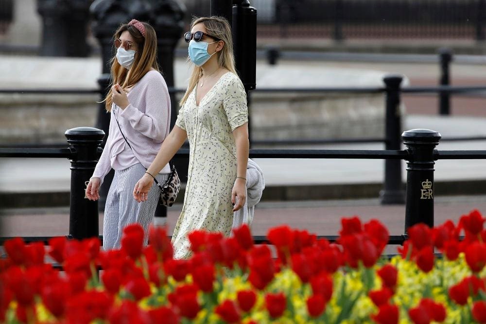 Duas mulheres usam máscaras protetoras enquanto passam pelas flores do lado de fora do Palácio de Buckingham, em Londres