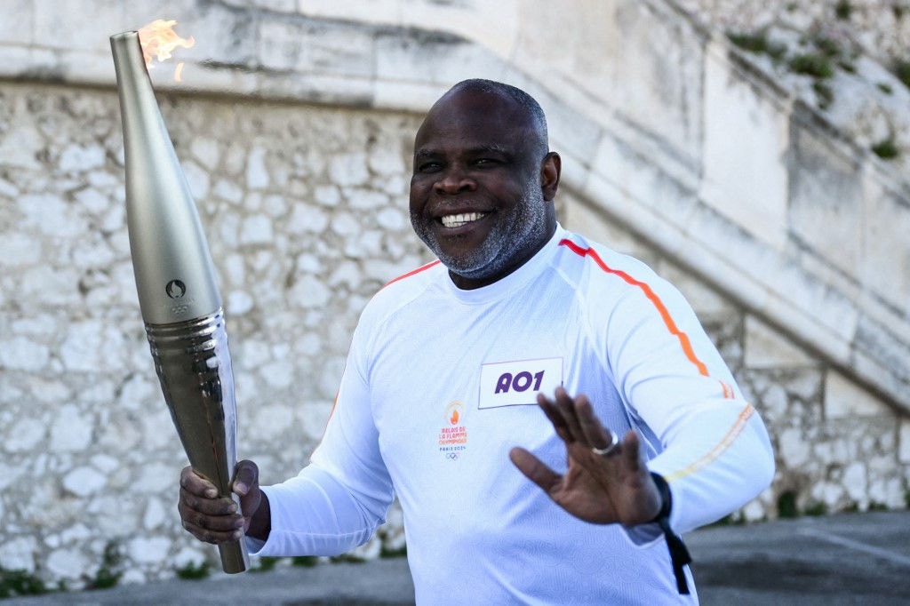 French former football player Basile Boli holds the Olympic Torch as part of the Olympic and Paralympic Torch Relays at the Notre Dame de la Garde Basilica, ahead of the Paris 2024 Olympic and Paralympic Games, in Marseille, southeastern France, on May 9, 2024. The transfer of the flame onshore from a 19th-century tall ship will mark the start of a 12,000-kilometre (7,500-mile) torch relay across mainland France and the country's far-flung overseas territories. (Photo by CHRISTOPHE SIMON / AFP)