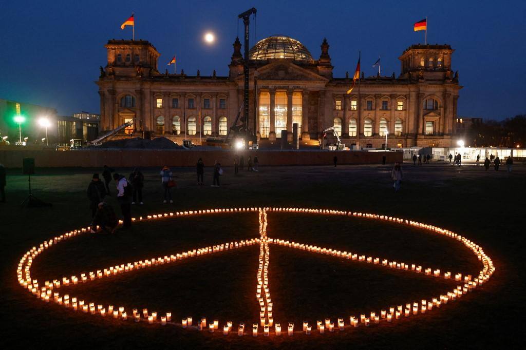 Pessoas formam um sinal de paz com velas antes de um comício que marca a véspera do segundo aniversário da invasão da Ucrânia pela Rússia, em frente ao Reichstag, em Berlim