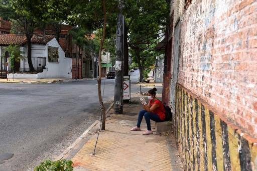 Uma mulher espera um ônibus em uma rua deserta em Assunção