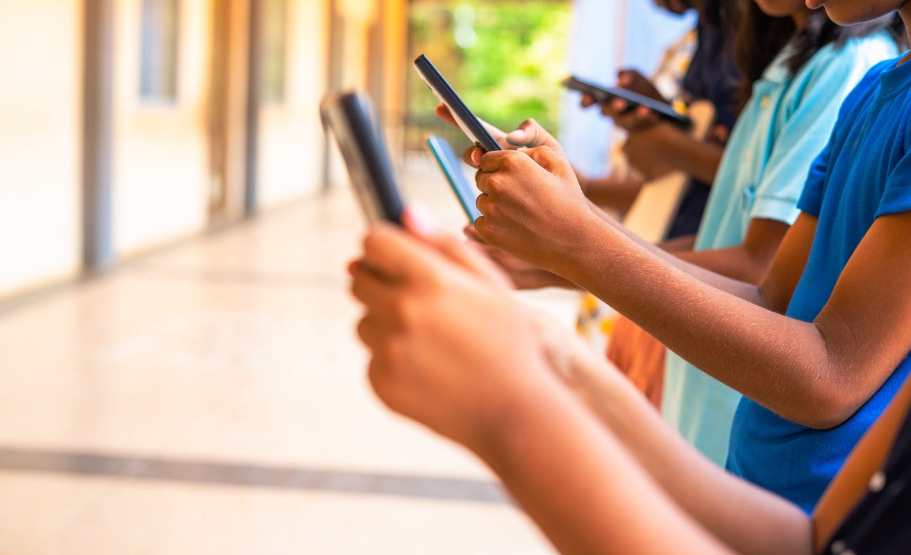 Close up shot, group of children hands busy using smartphone at school corridor - concept of social media, playing games, technology and education.