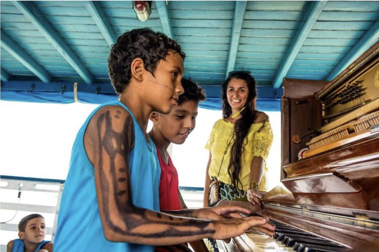 Cena do documentário 'Raízes: Um Piano na Amazônia', em que a pianista Carla Ruaro toca num barco enquanto navega por rios amazônicos para levar repertório local a comunidades ribeirinhas