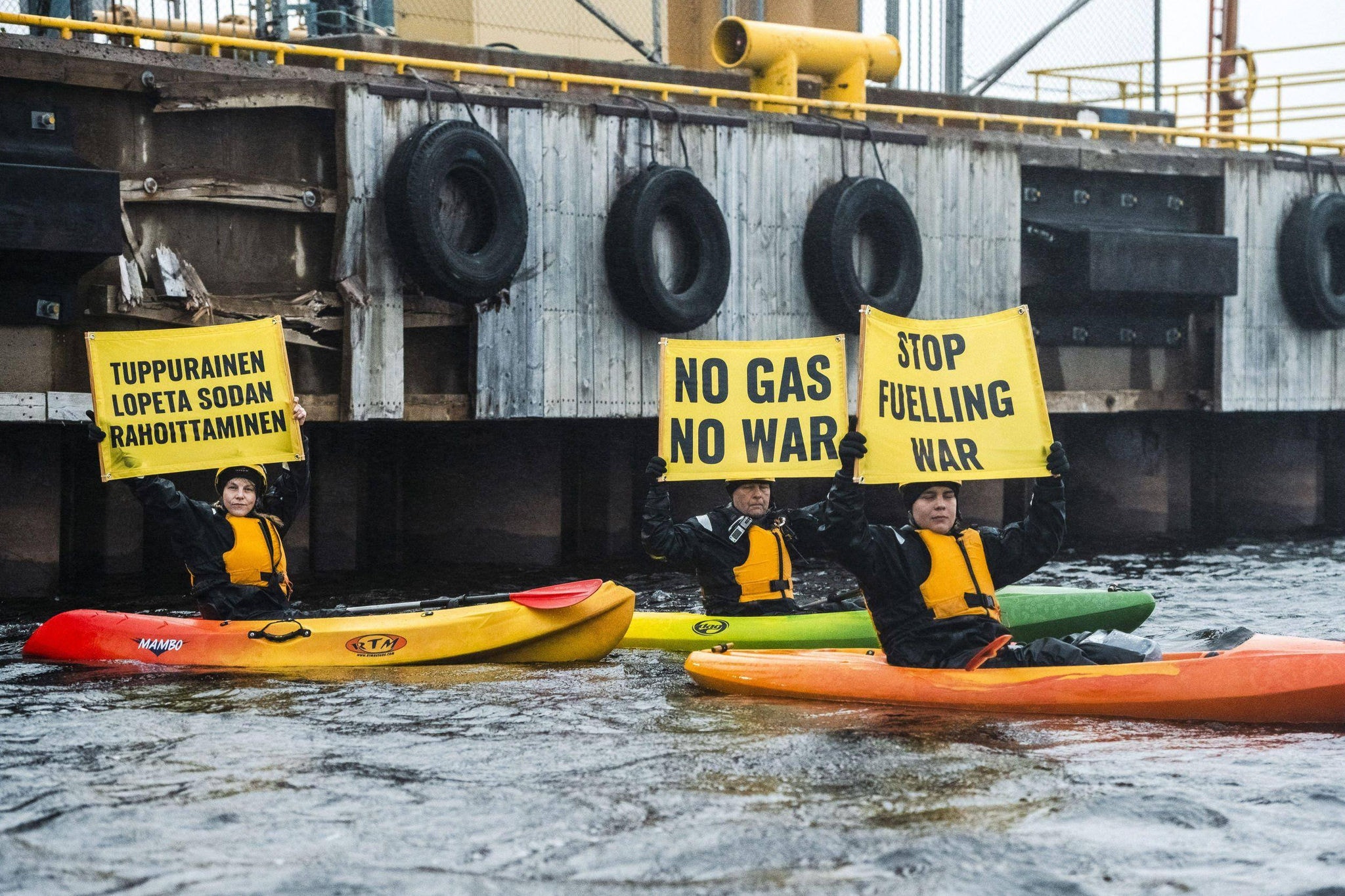 Ativistas do Greenpeace, em pequenos barcos, exibem faixas com dizeres "Stop Fueling War" e "No Gas No War" enquanto bloqueiam um carregamento de gás fóssil russo