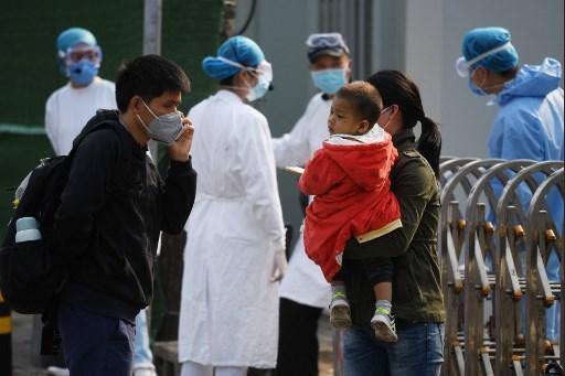Uma família espera entrar no hospital infantil enquanto fica perto da equipe do hospital (traseira) usando equipamento de proteção como medida de precaução contra o coronavírus COVID-19 em Pequim