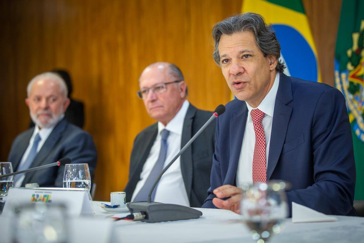 Ministro da Fazenda, Fernando Haddad, ao lado do vice-presidente, Geraldo Alckmin, e do presidente Lula em cerimônia no Palácio do Planalto
