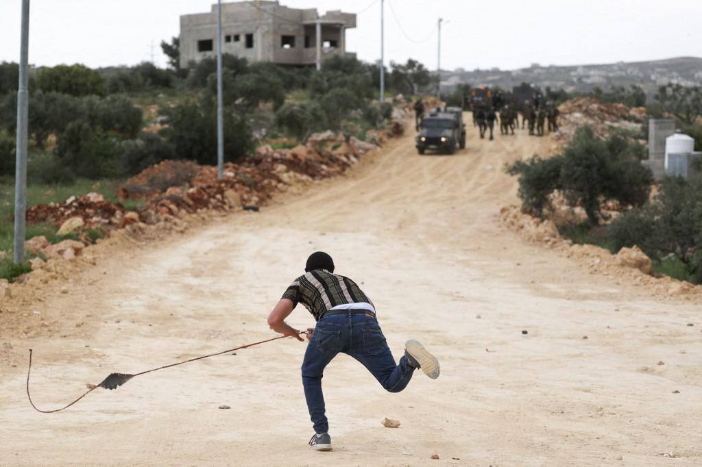 Palestino joga uma pedra contra forças israelenses 1042023