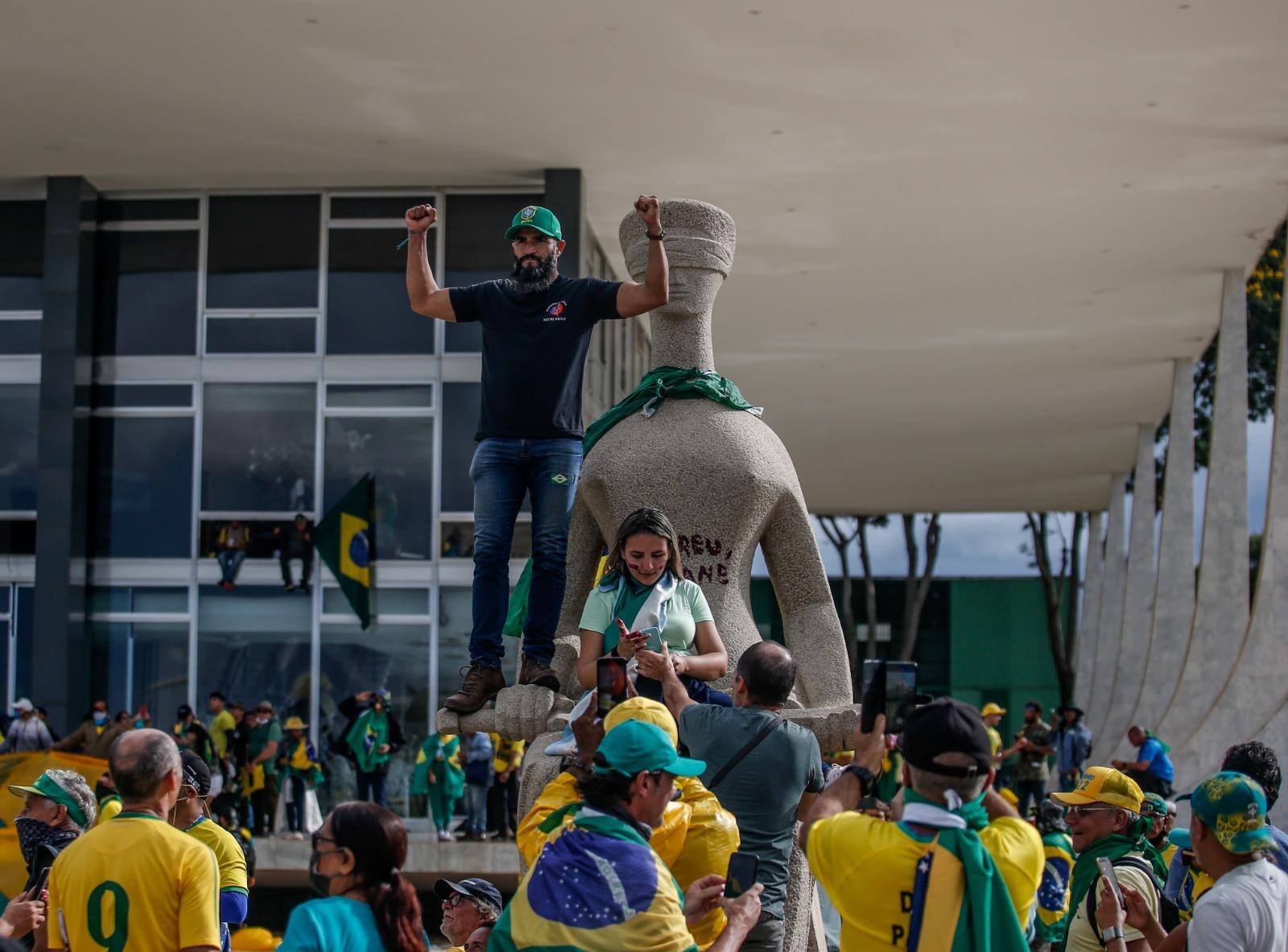 Mulher aparece sentada sob a estátua da Justiça pichada com "perdeu, mané" durante os atos criminosos de 8 de janeiro