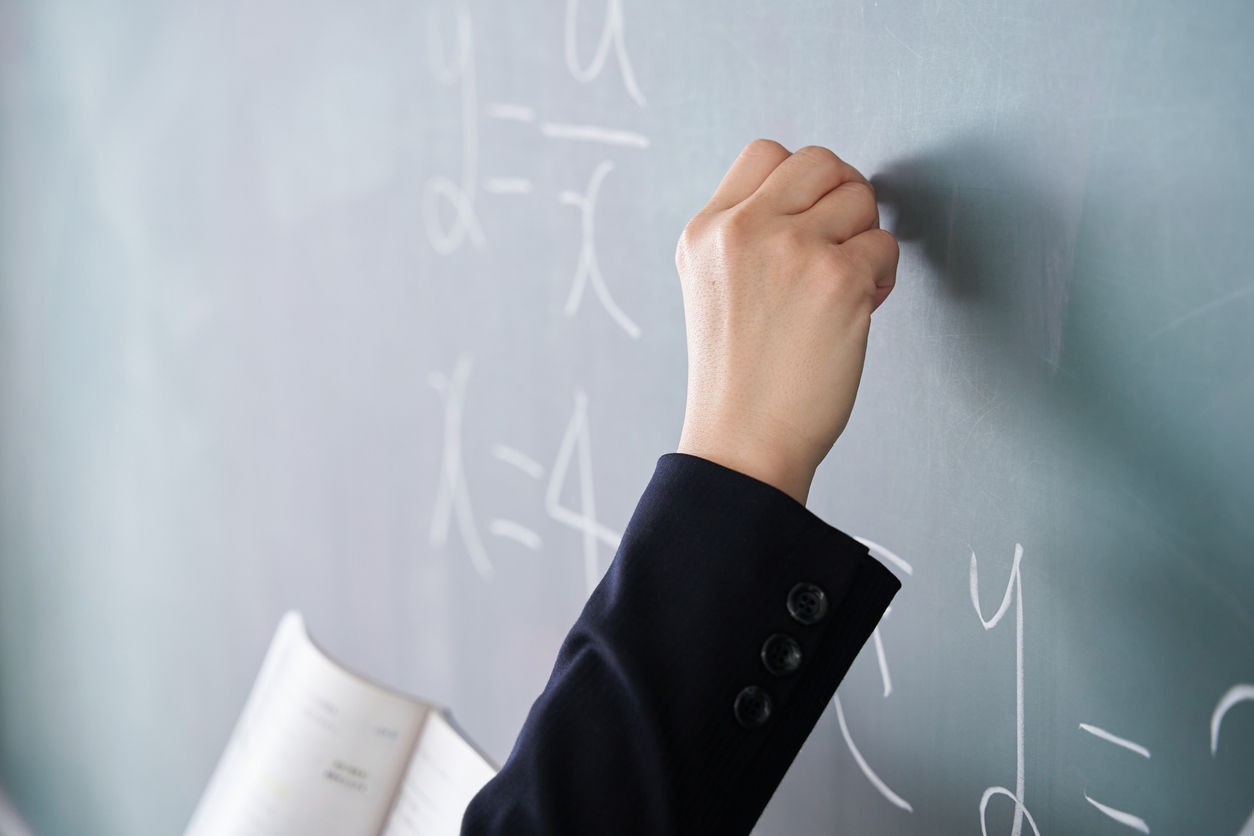 A Japanese woman teacher writes on the blackboard in her classroom