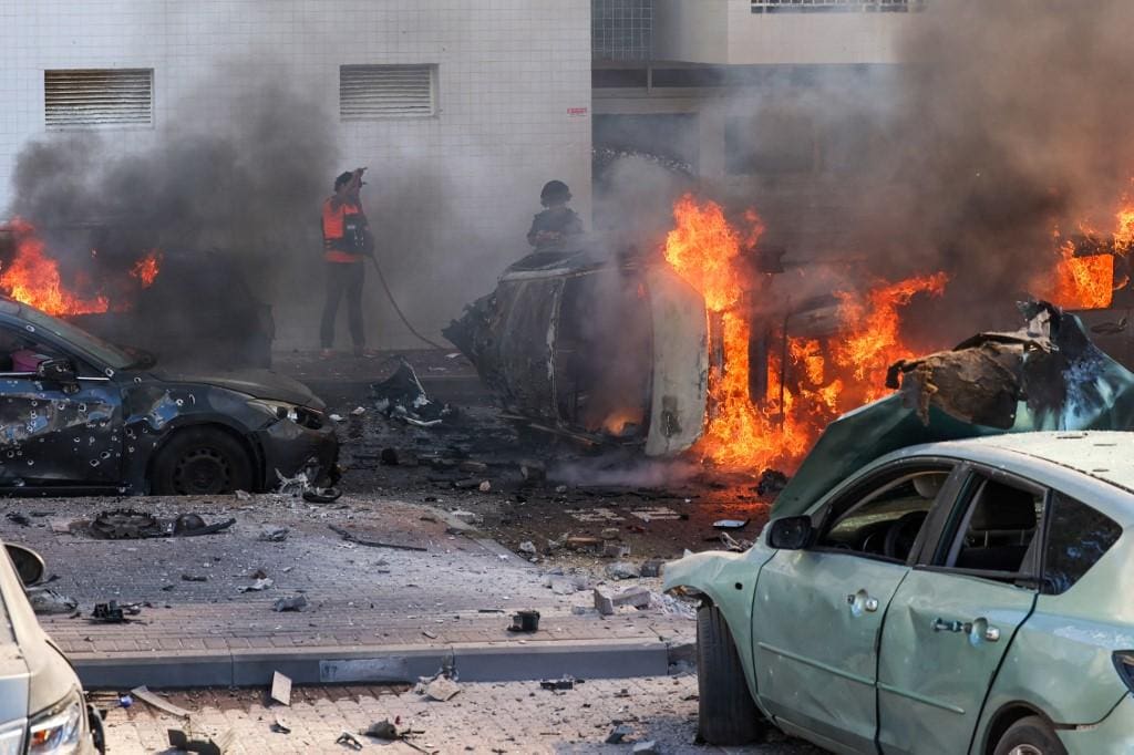 Pessoas tentam apagar fogo contra carros após um ataque com foguetes da Faixa de Gaza em Ashkelon, sul de Israel, em 7 de outubro de 2023