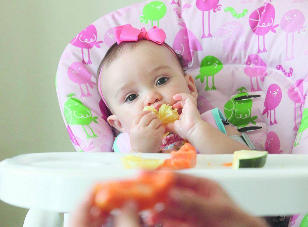 Jasmim, de 8 meses, leva os alimentos à boca sozinha, sob a supervisão da mãe