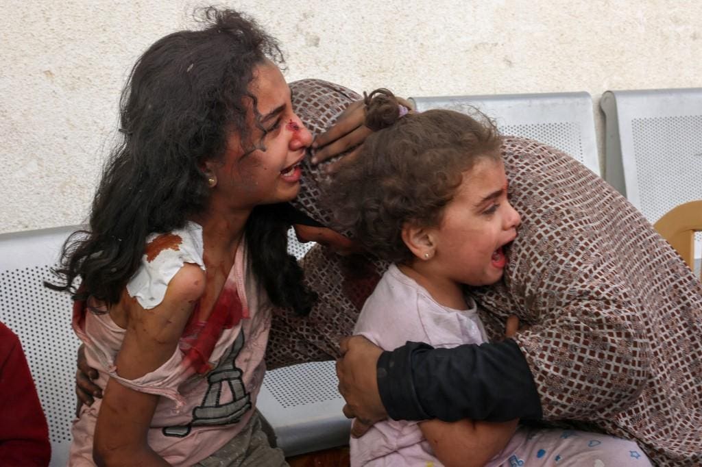 Mulher palestina consola filhas na porta de hospital enquanto esperam atendimento