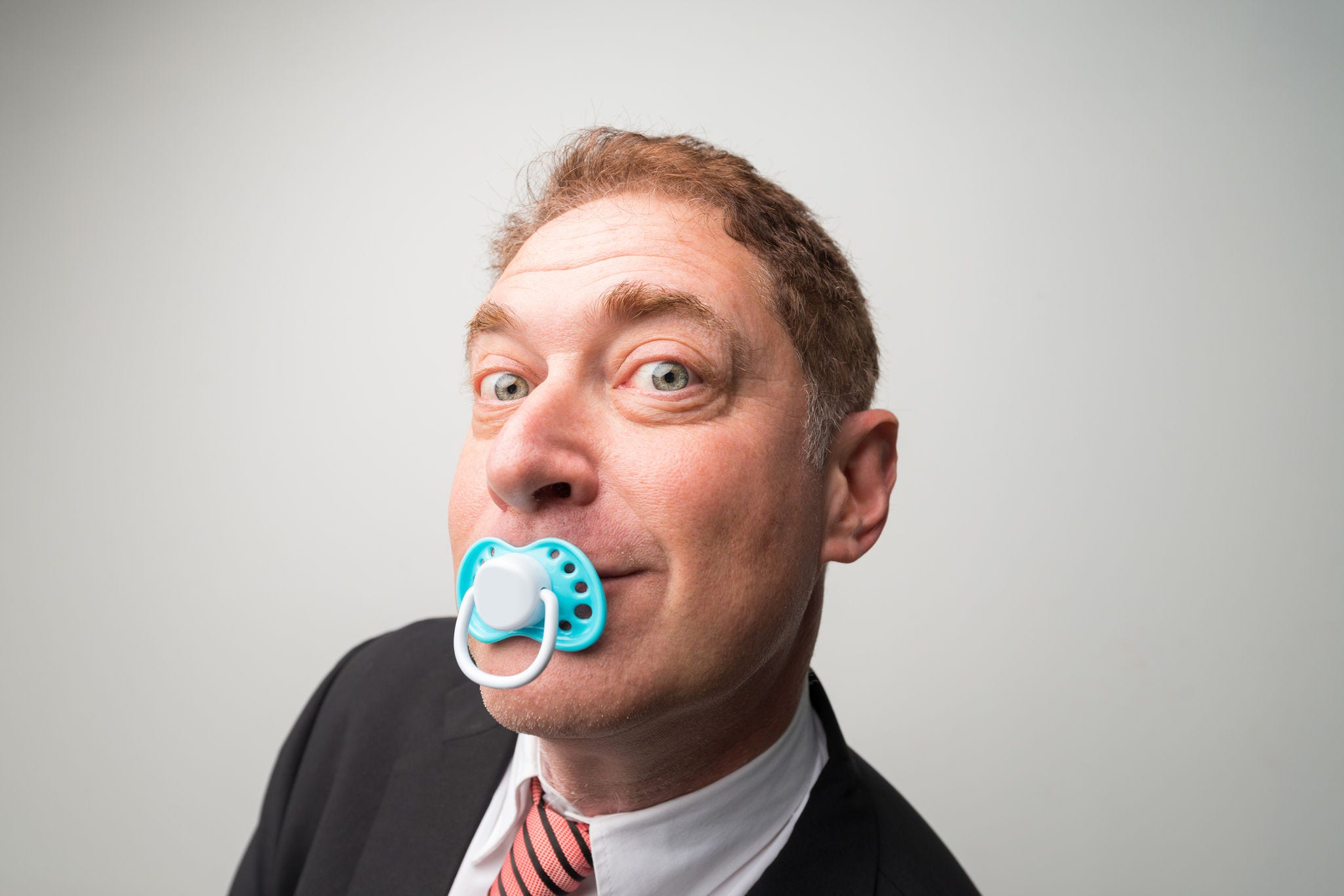 Curious businessman with a pacifier looking at the camera