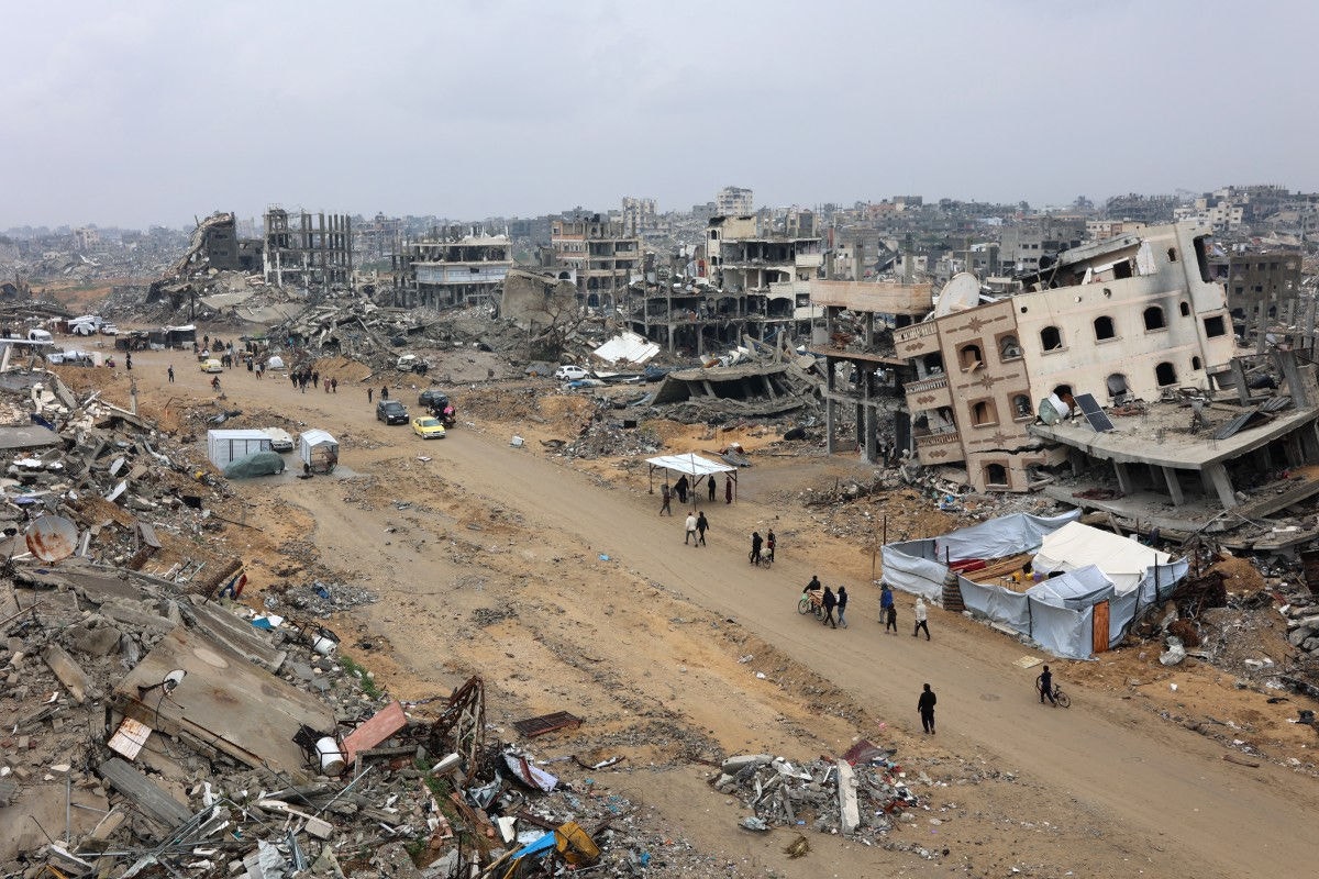 People walk amid collapsed buildings along Saftawi street in Jabalia in the northern Gaza Strip on February 5, 2025 during a ceasefire deal in the war between Israel and Hamas went into effect. Palestinian militant group Hamas lashed out on February 5, at President Donald Trump's shock proposal for the United States to take over the Gaza Strip and resettle its people in other countries, seemingly whether they want to leave or not. (Photo by Omar AL-QATTAA / AFP)