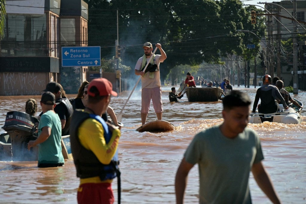 A man moves on in a SUP board following floodings due to heavy rains in Porto Alegre, Rio Grande do Sul state, Brazil on May 6, 2024. From top to bottom, rescuers scour buildings in Porto Alegre for inhabitants stuck in apartments or on rooftops as unprecedented flooding killed at least 78 people in the southern state, with dozens missing and some 115,000 forced to leave their homes. (Photo by NELSON ALMEIDA / AFP)