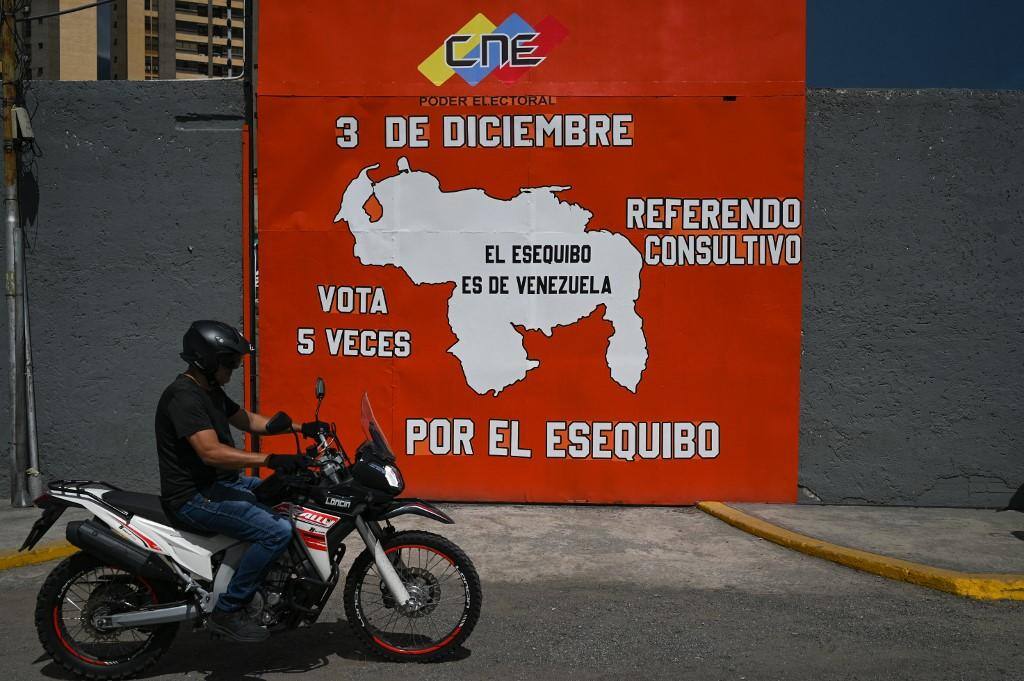 Um homem de moto em Caracas passa por um mural em campanha por um referendo para pedir aos venezuelanos que considerem anexar a região de Essequibo, administrada pela Guiana