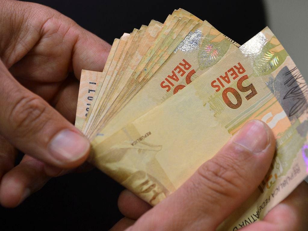 Mãos segurando notas de R$ 50. Imagem ilustrativa