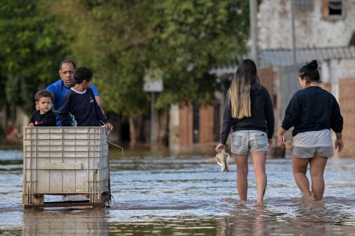 People walk along a flooded street in Eldorado do Sul, Rio Grande do Sul state, Brazil, on May 9, 2024. Teams raced against the clock Thursday to deliver aid to flood-stricken communities in southern Brazil before the arrival of new storms forecast to batter the region again. Some 400 municipalities have been affected by the worst natural calamity ever to hit the state of Rio Grande do Sul, with at least 107 people dead and hundreds injured. (Photo by Nelson ALMEIDA / AFP)